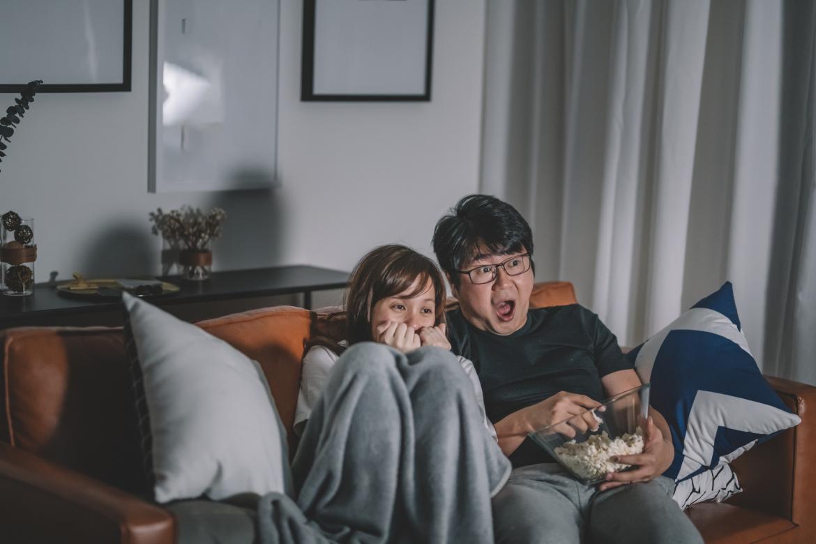 Una pareja de origen chino asiático está viendo un programa de terror en la televisión por la noche, durante el fin de semana, sentados en el sofá de la sala de estar.