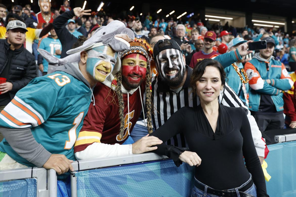 La presidenta de la Comunidad de Madrid, Isabel Díaz Ayuso posa junto a varios aficionados antes del partido de liga regular de la Liga de Fútbol Americano (NFL) que este domingo disputan los equipos Miami Dolphins (d) y Washington Commanders en el Estadio Santiago Bernabéu.