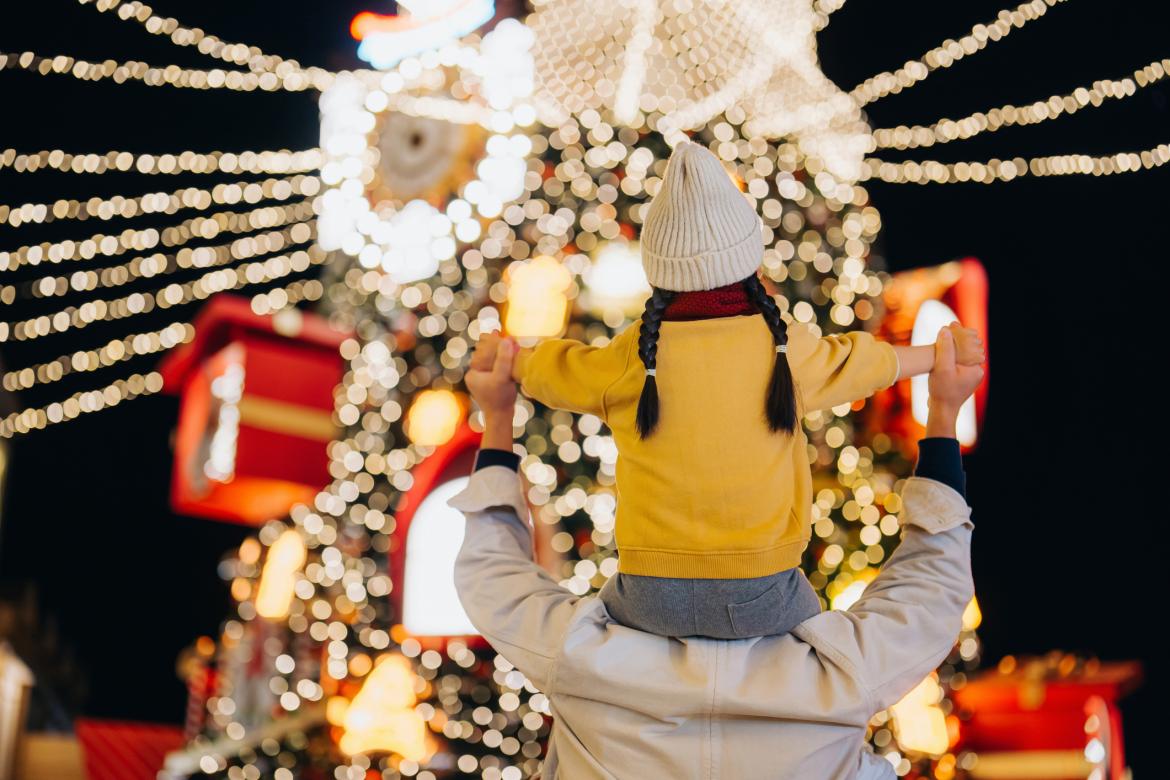 Vista trasera de un joven padre asiático cargando a su pequeña hija a hombros frente a un árbol de Navidad iluminado al aire libre. Compartiendo un momento feliz. Estilo de vida familiar. Disfrutando del ambiente navideño. Ambiente festivo. ¡Ya llegó la Navidad!