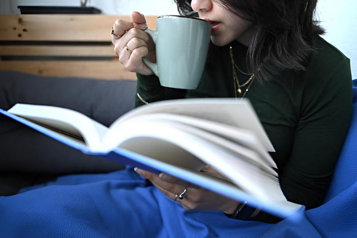 Una mujer lee un libro mientras bebe una taza de café