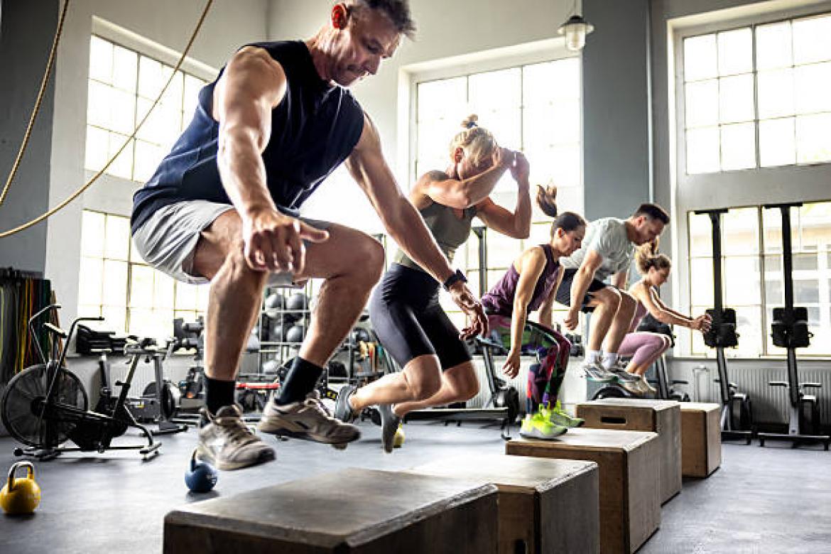 Men and women jump onto wooden boxes together, building strength, speed, and explosive power in a group session.