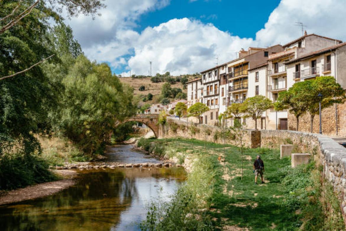 Covarrubias, Burgos Province, Castilla y León, España, September 18, 2021: Outside the walls, man with dog at the walk along the banks of the Arlanza river. Covarrubias, located 40 kilometers southeast of Burgos, is undoubtedly one of the most beautiful towns in Spain. Covarrubias is now a town that stands out above all for its traditional architecture built with wooden and adobe structures. White facades and wooden frames, well cared for, which form a set of great beauty.