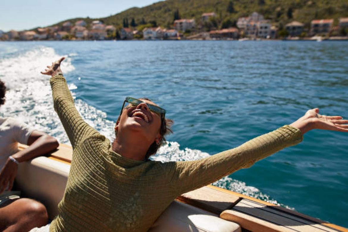Happy young woman with arms raised in motorboat enjoying sunny day
