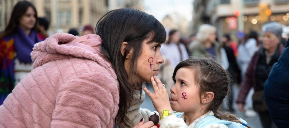 Una niña le pinta la cara a una mujer durante la manifestación del 8 de marzo de 2023 en Barcelona.
