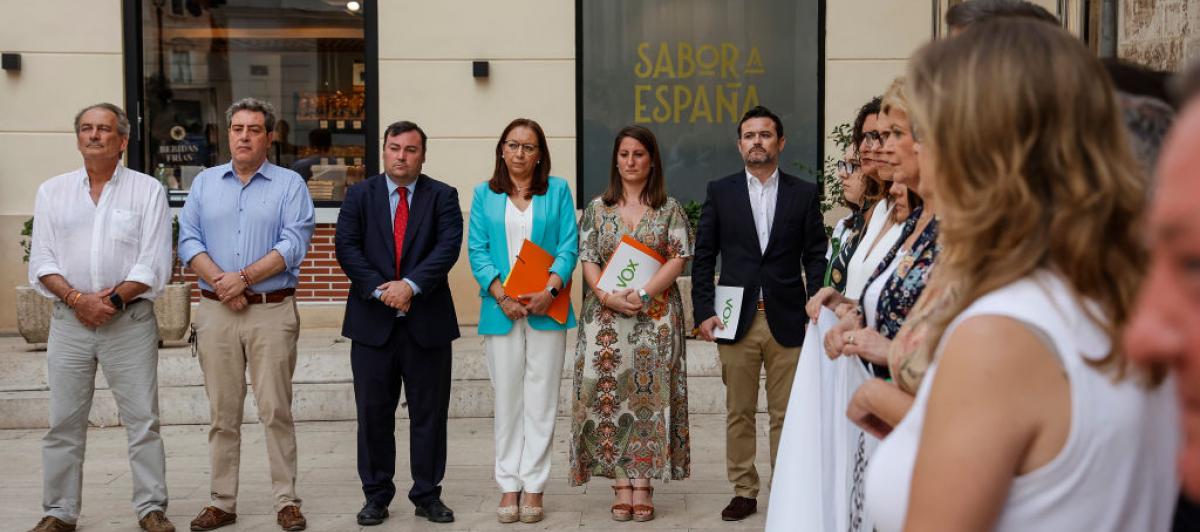 Representantes de Vox, al fondo, separados de la pancarta que denuncia el crimen machista de Antella, en primer término.