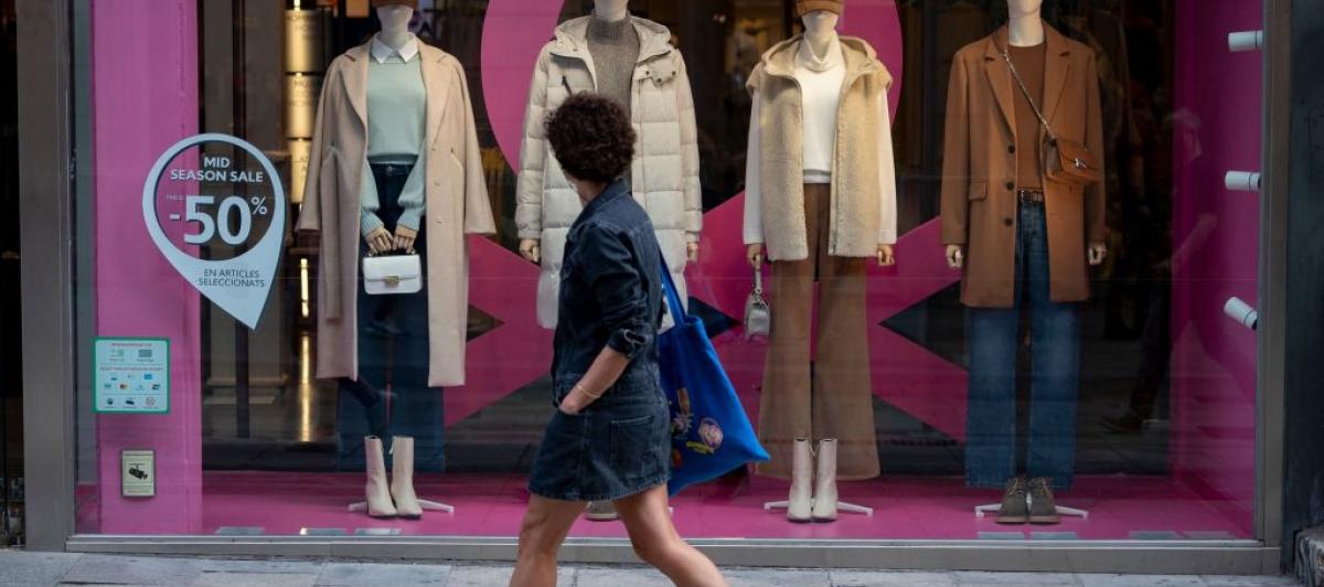 Una mujer pasea en un día de calor de octubre y mira a un escaparate con abrigos