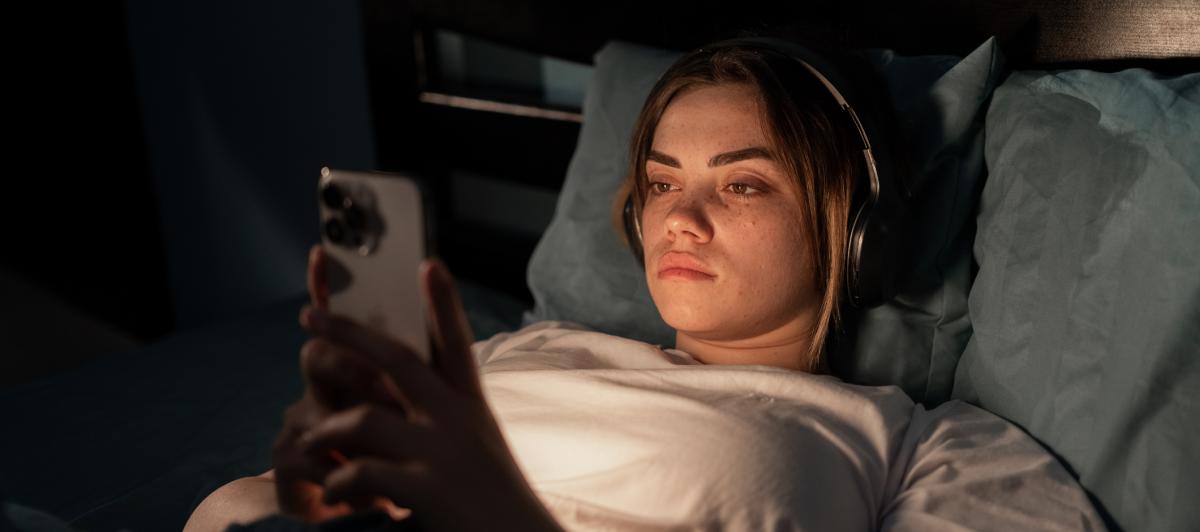 Imagen de archivo de una mujer joven en la cama con un móvil.