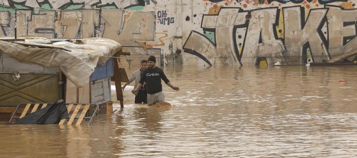 Dos personas vadean un terreno de chabolas inundado junto a la V-30 a causa de las lluvias torrenciales de las últimas horas.
