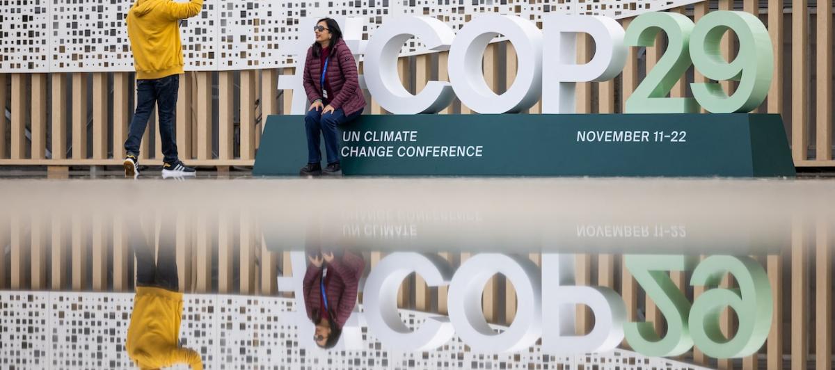 Dos personas se hacen fotos a la entrada del edificio en el que se celebrará la cumbre de la ONU sobre el cambio climático en Bakú.