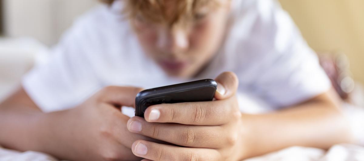 Un adolescente consulta su teléfono móvil tumbado en la cama.