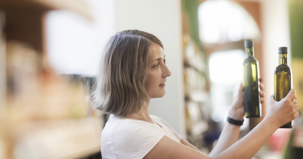 Imagen de archivo de una mujer comparando dos botellas de aceite de oliva en un supermercado.