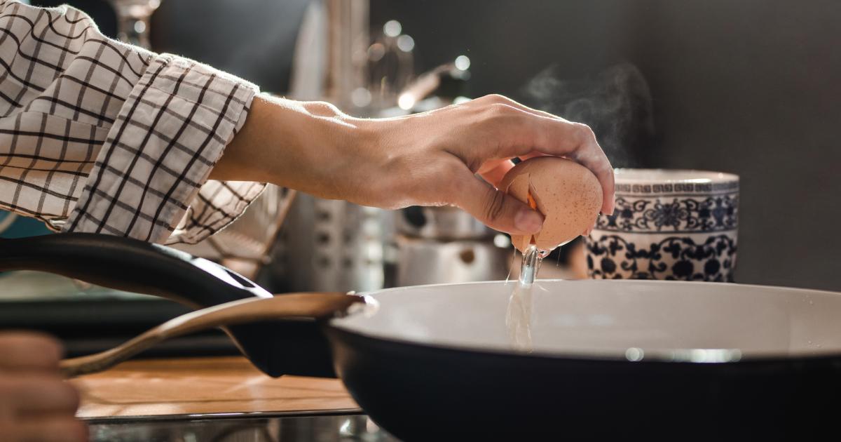 Una persona cascando un huevo en el borde de la sartén.