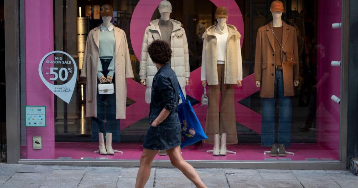 Una mujer pasea en un día de calor de octubre y mira a un escaparate con abrigos