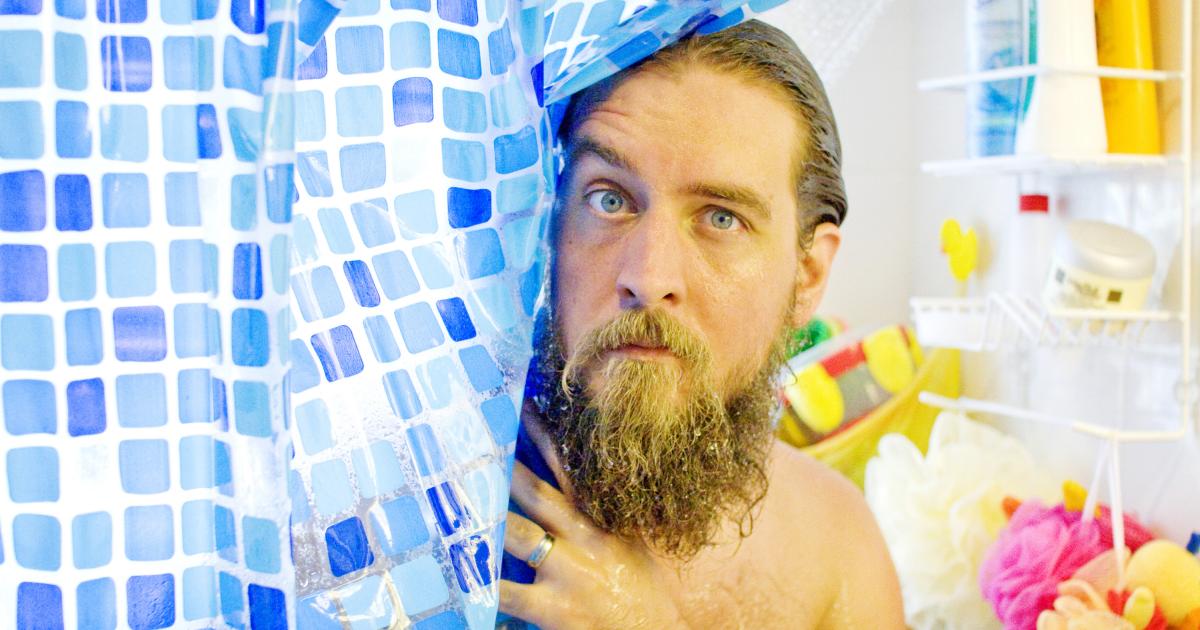 Un hombre se asoma por las cortinas de la ducha.