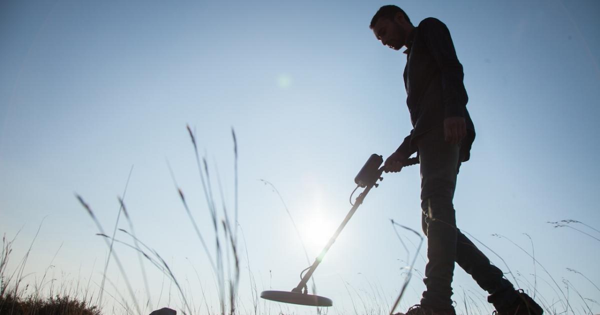 Un hombre busca los restos de un tesoro valiéndose de un detector de metales.