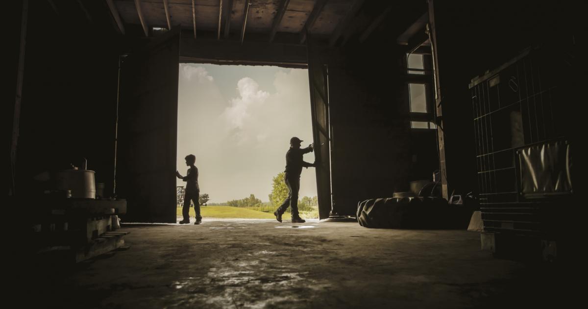 Imagen de un adulto y un joven abriendo el portón de un cobertizo o granero.