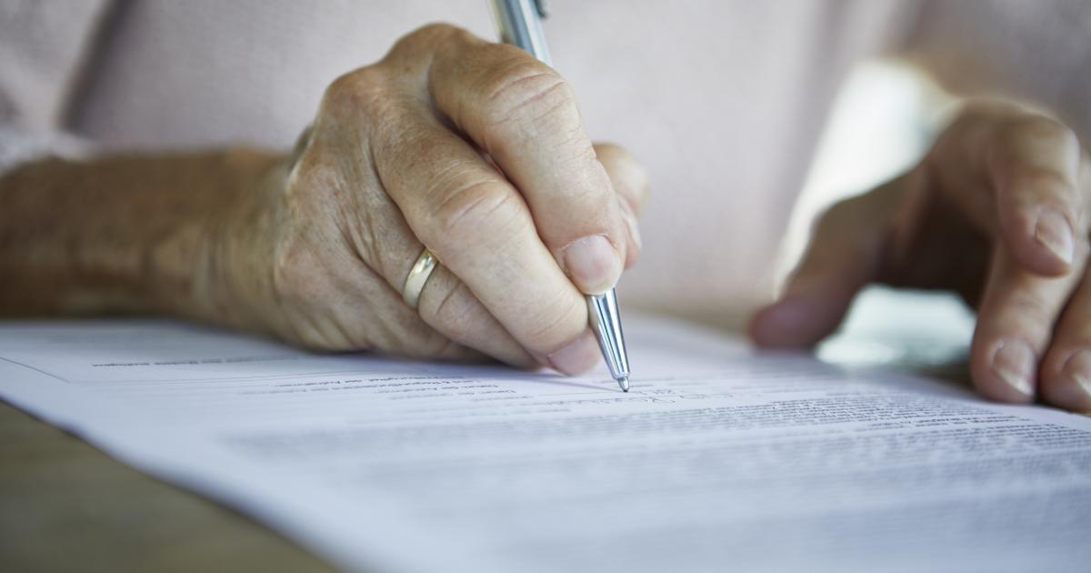 Imagen de una persona mayor firmando un documento.