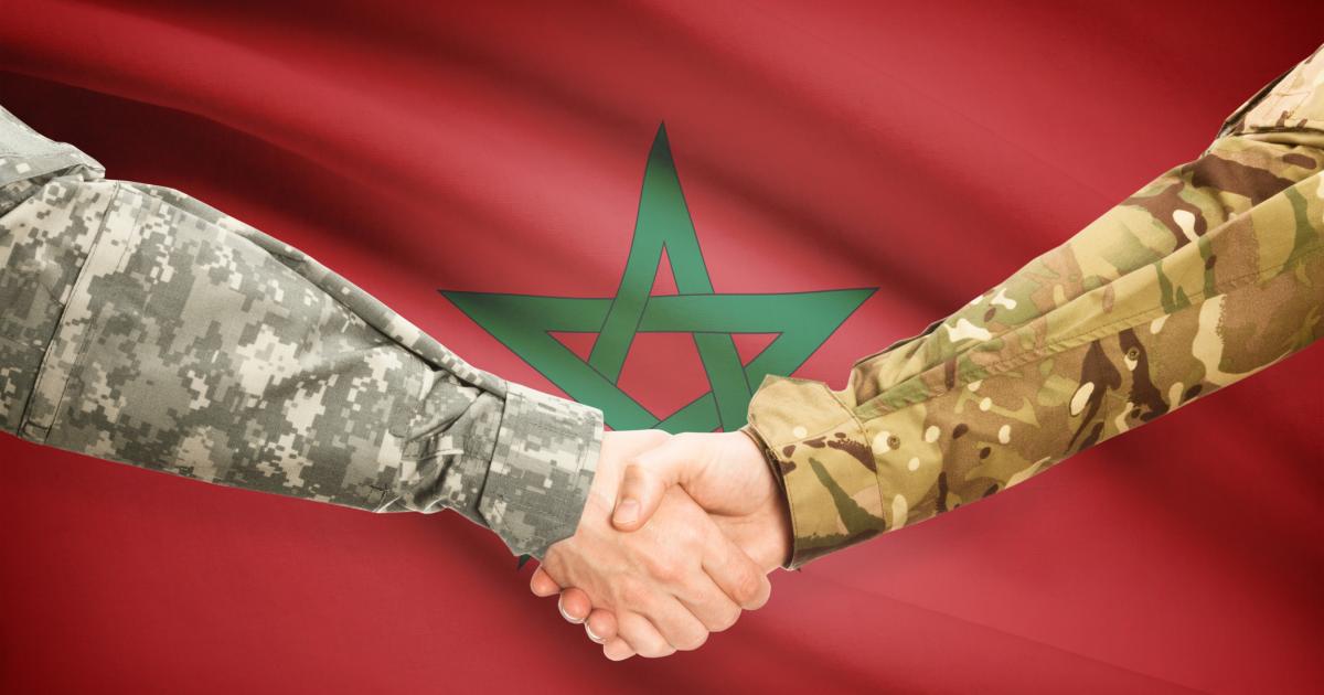 Ilustración digital de dos hombres uniformados estrechándose la mano ante la bandera de Marruecos.