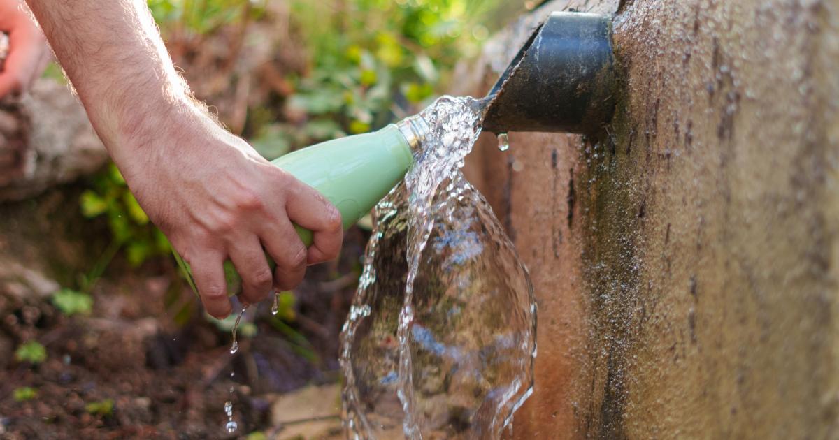 Una persona llenando de agua una botella de aluminio