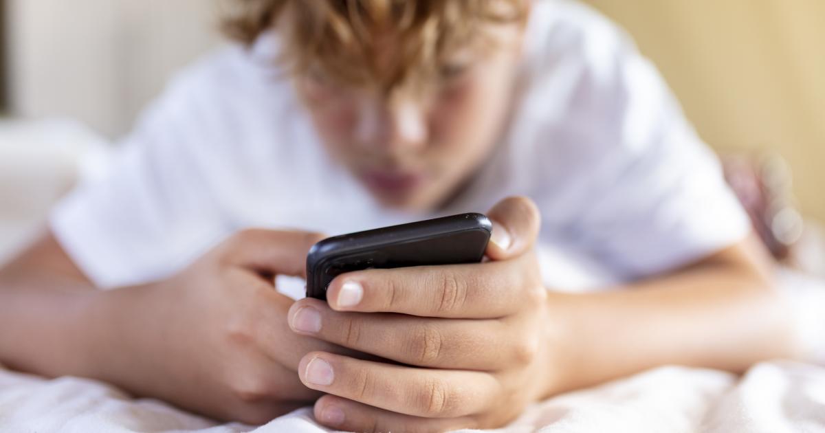 Un adolescente consulta su teléfono móvil tumbado en la cama.