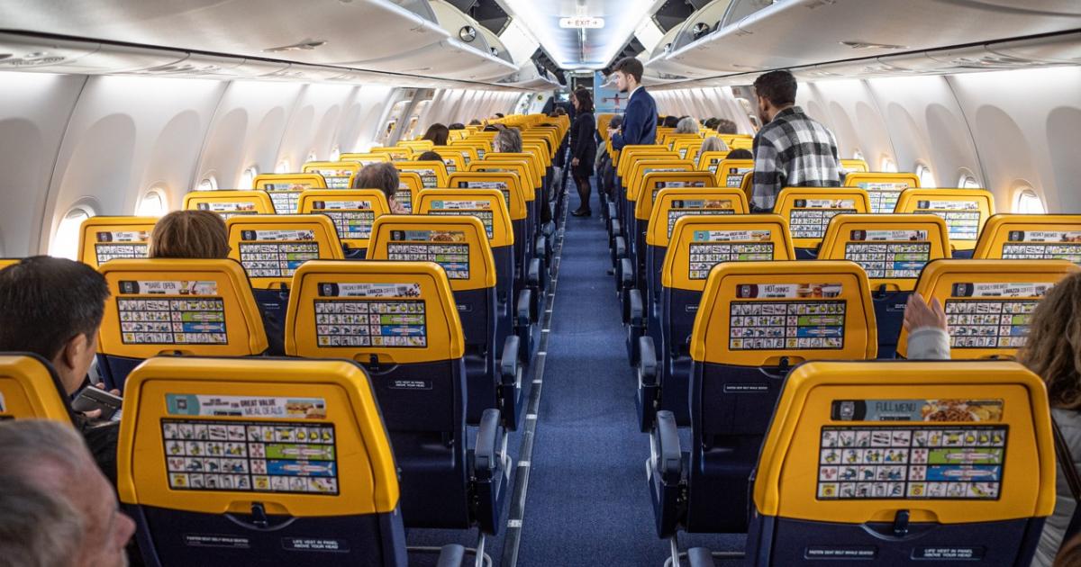Interior de un avión de Ryanair con pasajeros sentados y tripulación atendiendo en cabina.