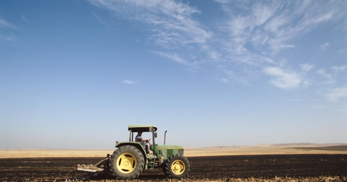 Tractor verde arando un campo bajo un cielo despejado.