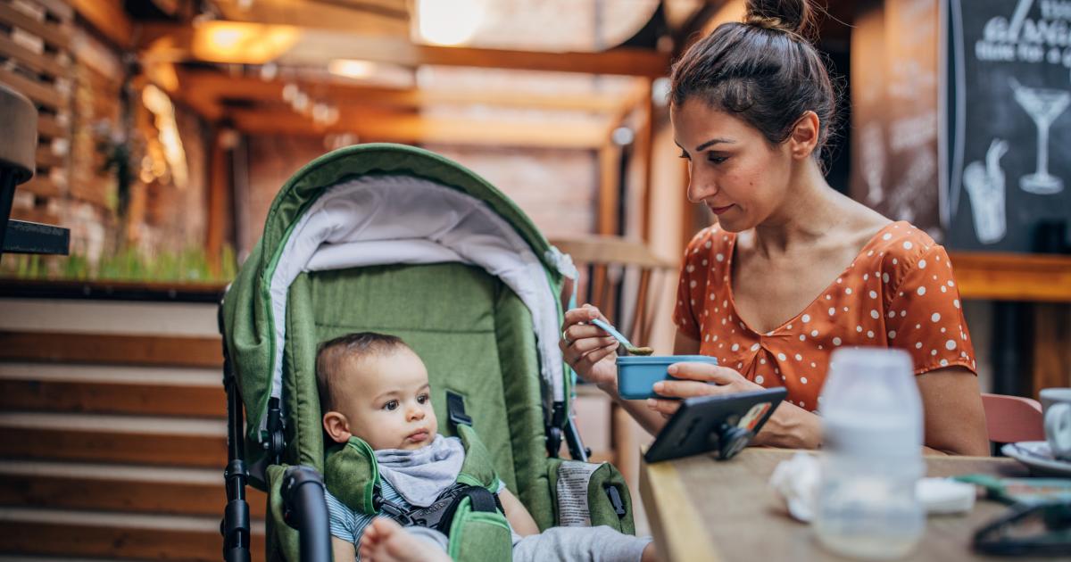 Mujer dando de comer a su hijo pequeño mientras está sentada en una cafetería.