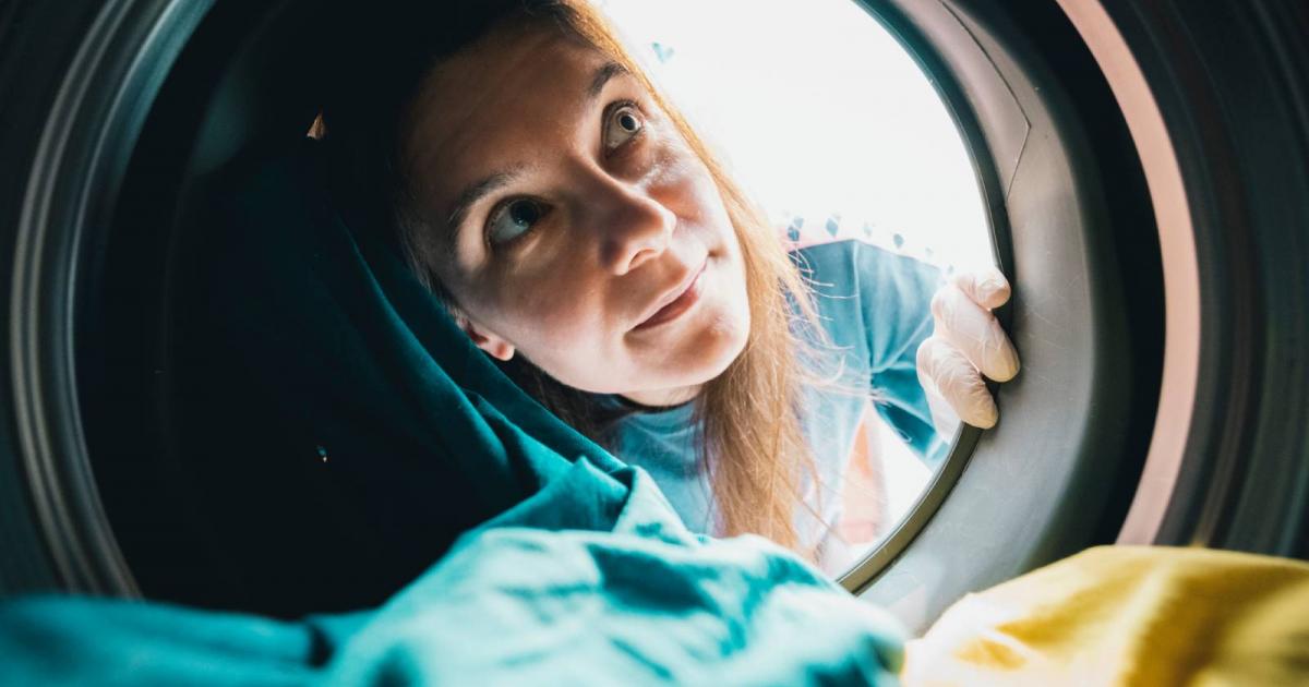 Una mujer con guantes observa el interior de una lavadora