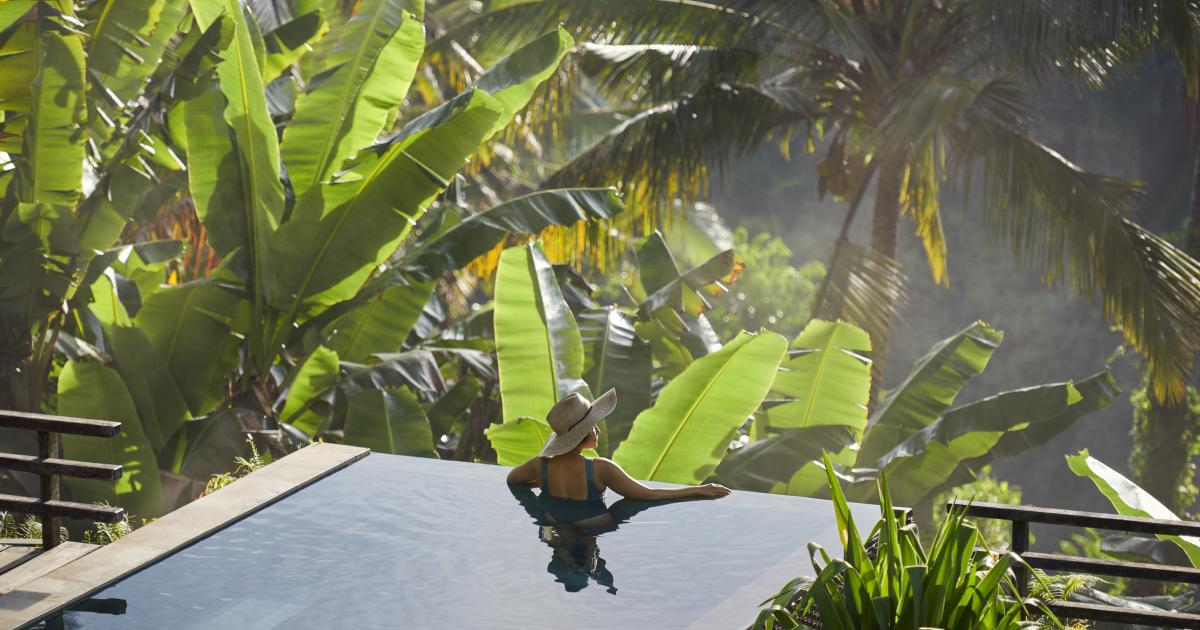 Mujer disfrutando de una hermosa piscina privada en una villa de lujo en Ubud (Bali, Indonesia), rodeada de árboles y plantas tropicales, situada al borde de un valle brumoso.