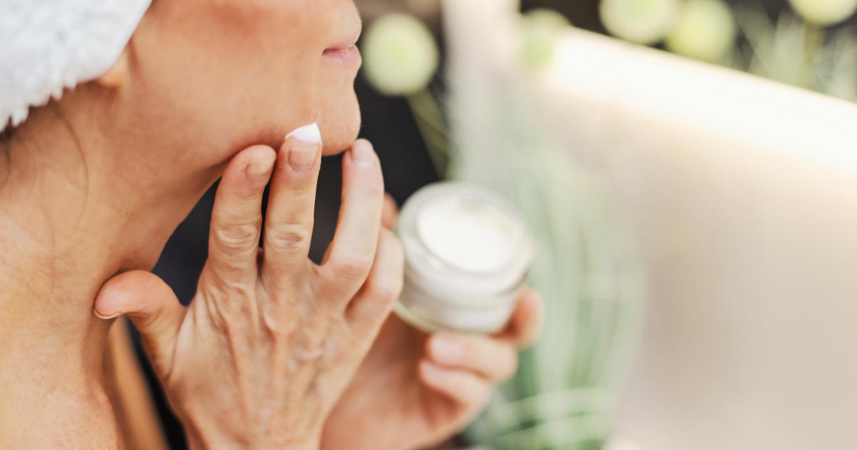 Una mujer aplicándose crema hidratante frente al espejo