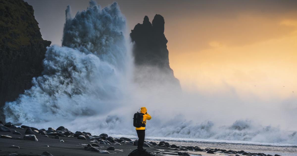 Explorador de pie en una costa rocosa con olas espectaculares y el atardecer como telón de fondo en Islandia.