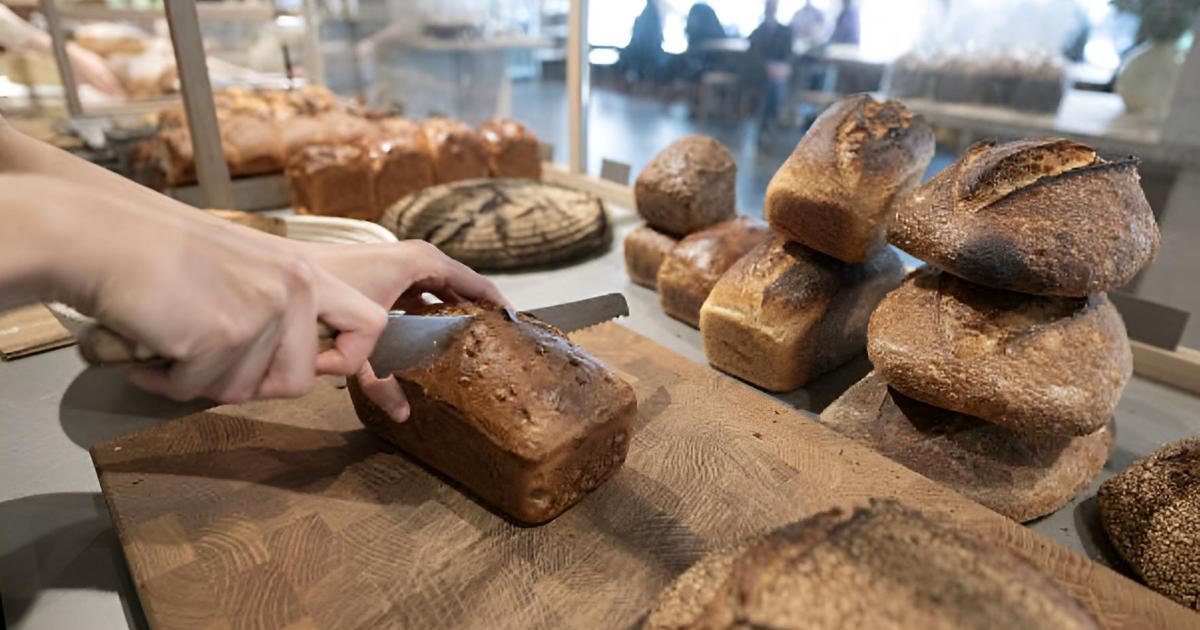Un empleado cortando pan recién hecho para venderlo