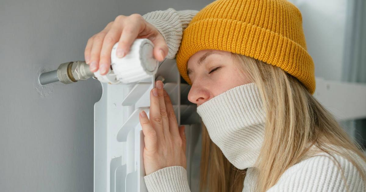 Mujer con sombrero calentándose mientras está sentada en el suelo cerca del radiador