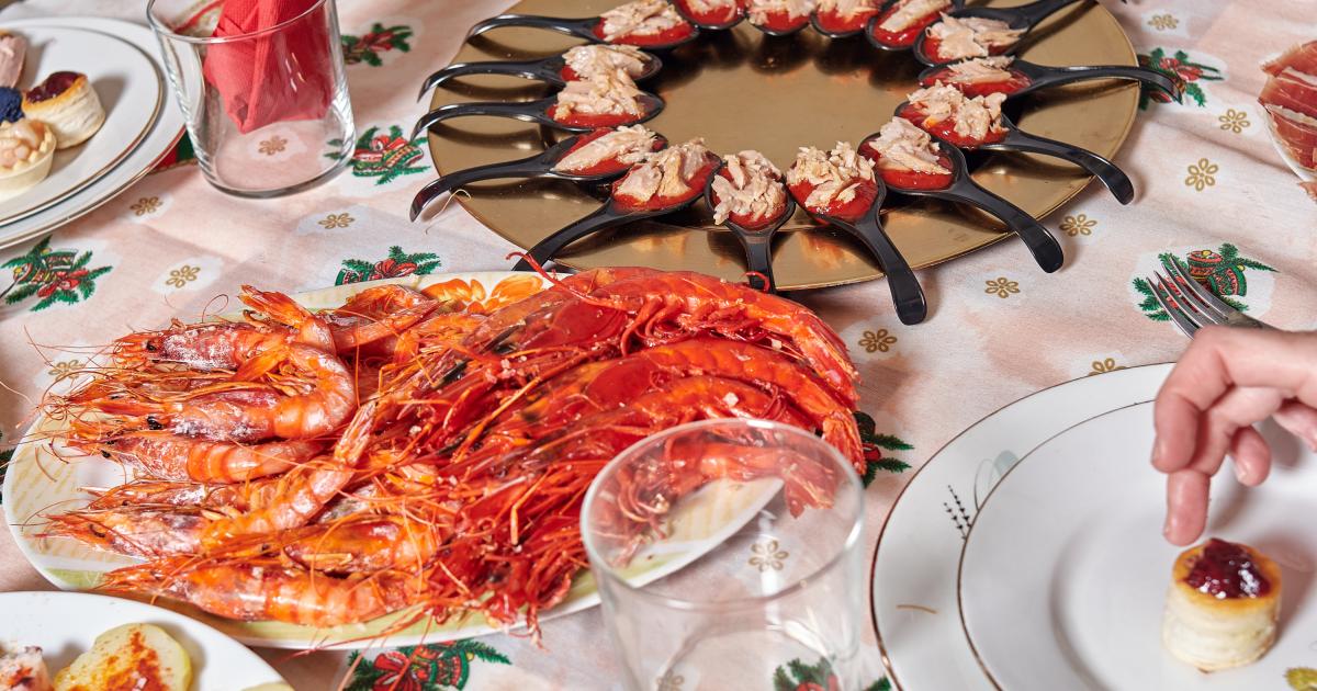 Plato de camarones a la plancha y plato de aperitivos sobre una mesa con mantel con motivos navideños. preparación de la cena navideña familiar.
