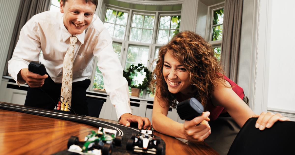 Imagen de dos personas adultas, jugando con el Scalextrix, sin que nadie repare en que no hay niños en la habitación.