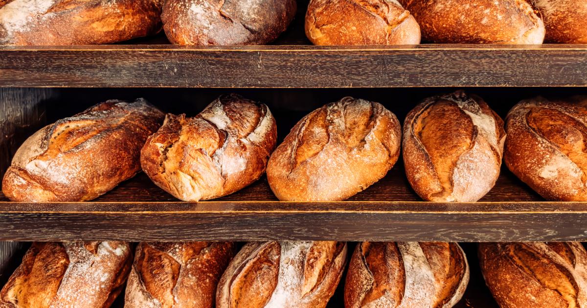 Varias hogazas de pan rústico en estantes de madera de una panadería