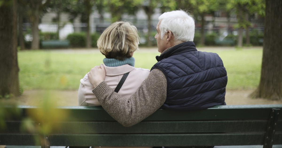 Una pareja de ancianos sentada en un banco público en un jardín público.