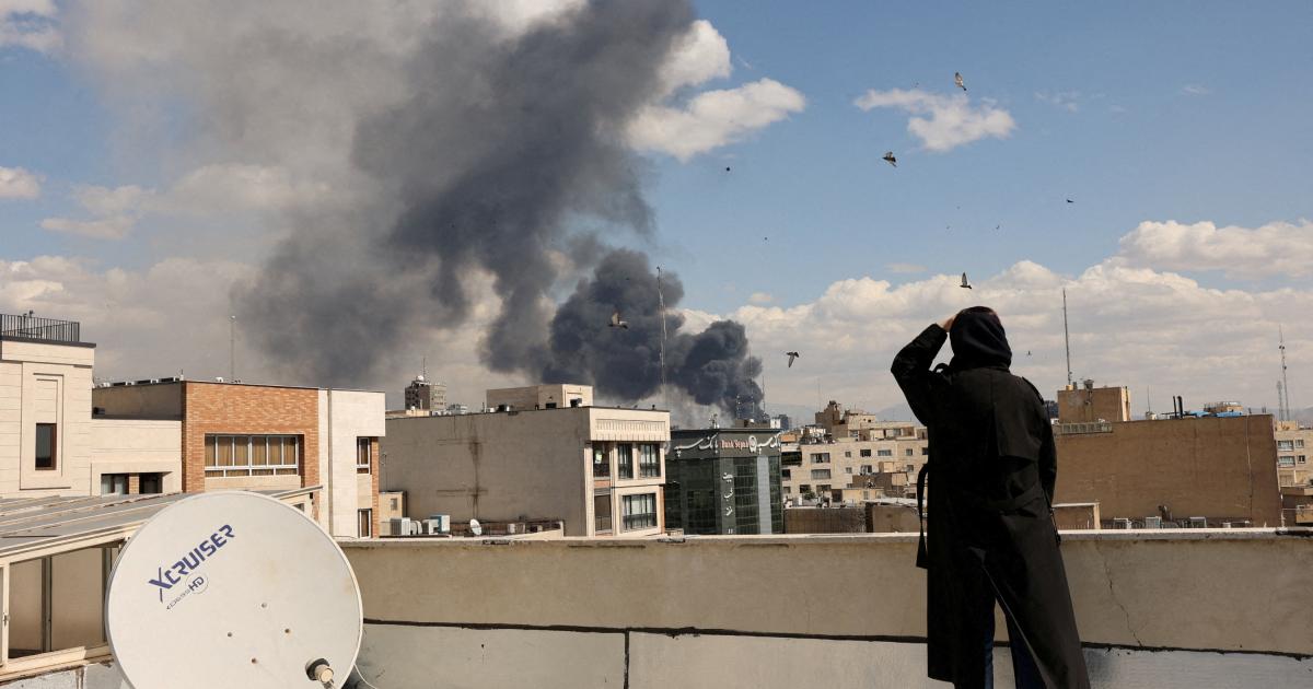 Una mujer, desde una terraza, ve el humo de los bombardeos en Teheran