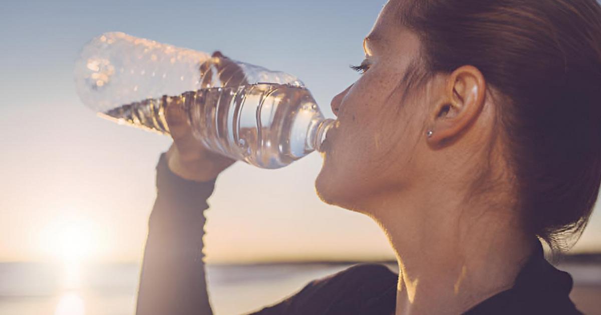 Una mujer bebiendo agua junto al mar