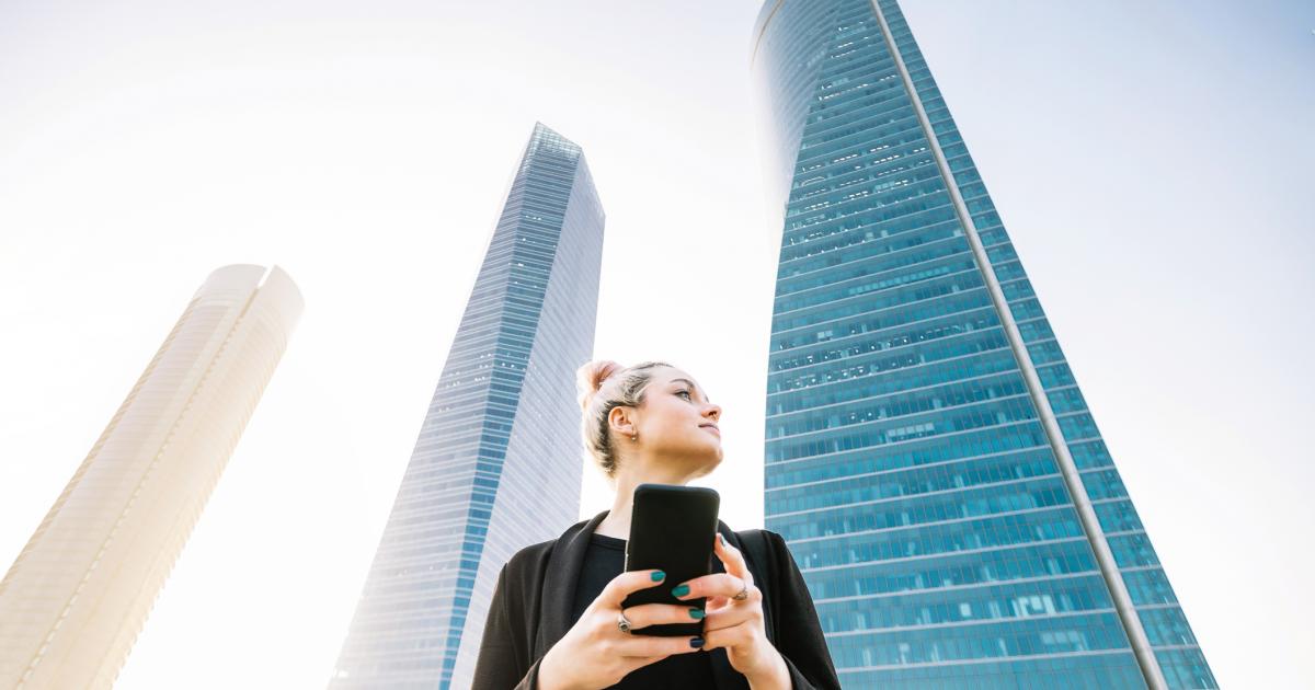 Horizontal mid waist view of blonde young woman typing on phone in financial city in Madrid. People and business lifestyles