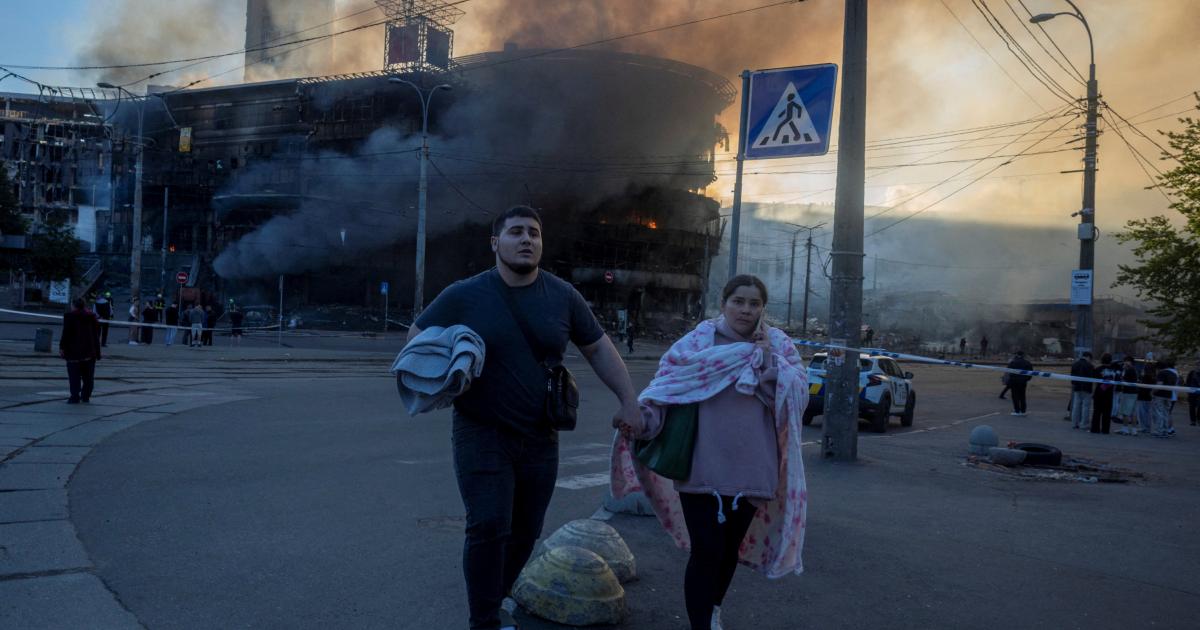 Varias personas caminan cerca de un edificio en llamas, al salir de un refugio tras los ataques nocturnos con misiles y drones rusos, el 24 de mayo de 2026, en Kiev.