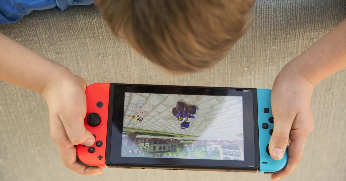 Un niño jugando a la Nintendo Switch: vista cenital, se le ve la coronilla con pelo del niño apoyado sobre un sofá y la Switch encendida
