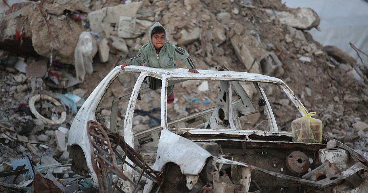 Un niño juega sobre un coche destrozado por los ataques de Israel, entre edificios hundidos, en el campo de refugiados de Bureij, en Deir al-Balah (Gaza), el 17 de enero de 2026.