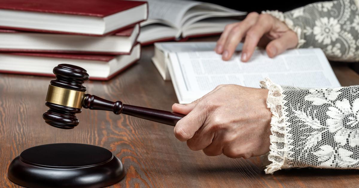 Primer plano de las manos del juez golpeando el mazo, con la toga con puños de encaje y los libros de derecho sobre el escritorio en la sala del tribunal, en una imagen de archivo.