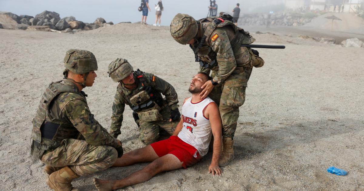 Soldados españoles rescatan a un migrante herido en la playa, tras la llegada masiva a pie y por mar desde Marruecos, en Ceuta, el 1 de agosto de 2026.