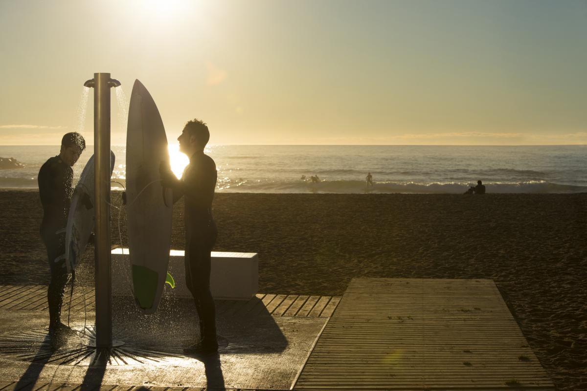 Dos surferos en la ducha de una playa al atardecer.