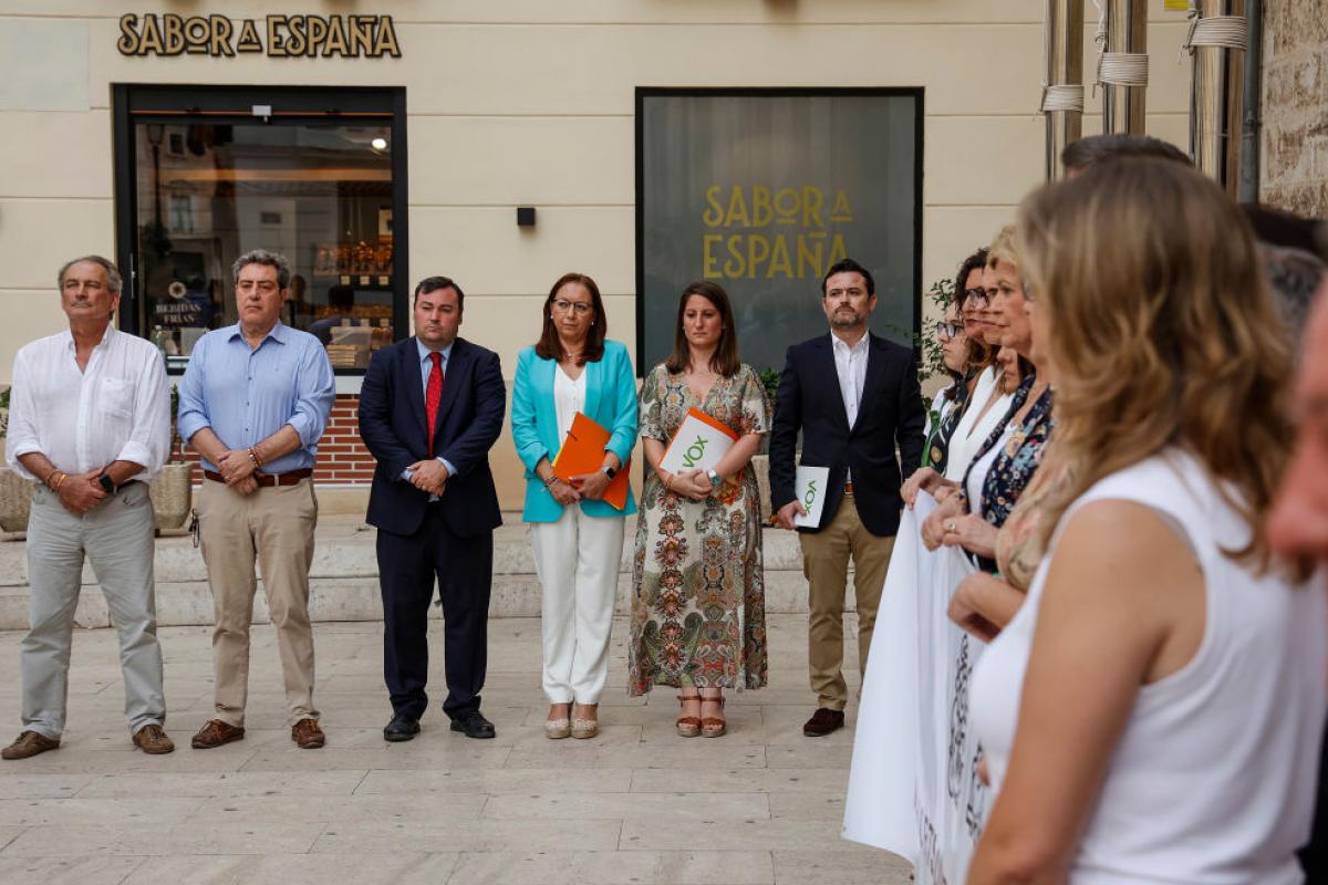 Representantes de Vox, al fondo, separados de la pancarta que denuncia el crimen machista de Antella, en primer término.