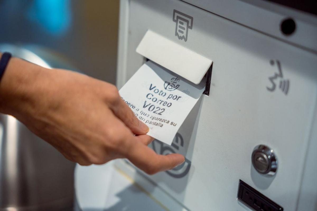 Una persona retirando el resguardo para votar por correo en una oficina.