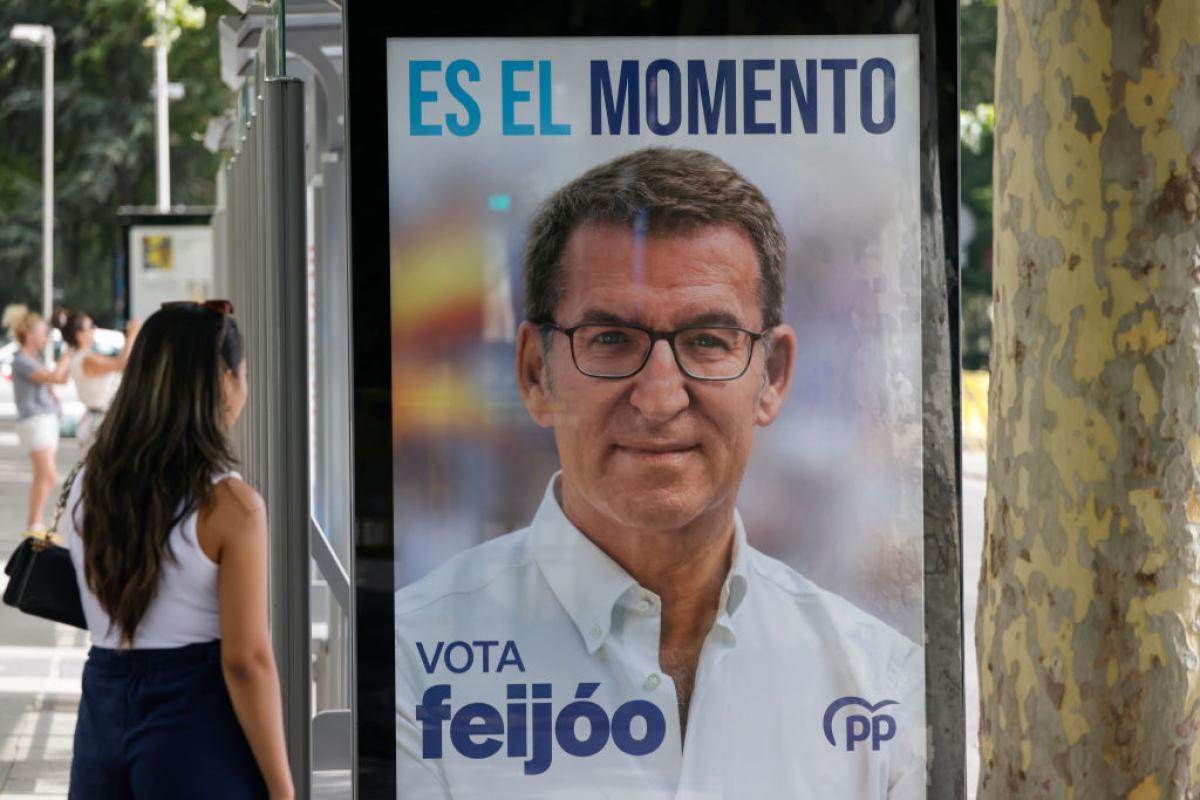 Una mujer junto a una marquesina de una para de autobús con propaganda electoral de Alberto Núñez Feijóo.