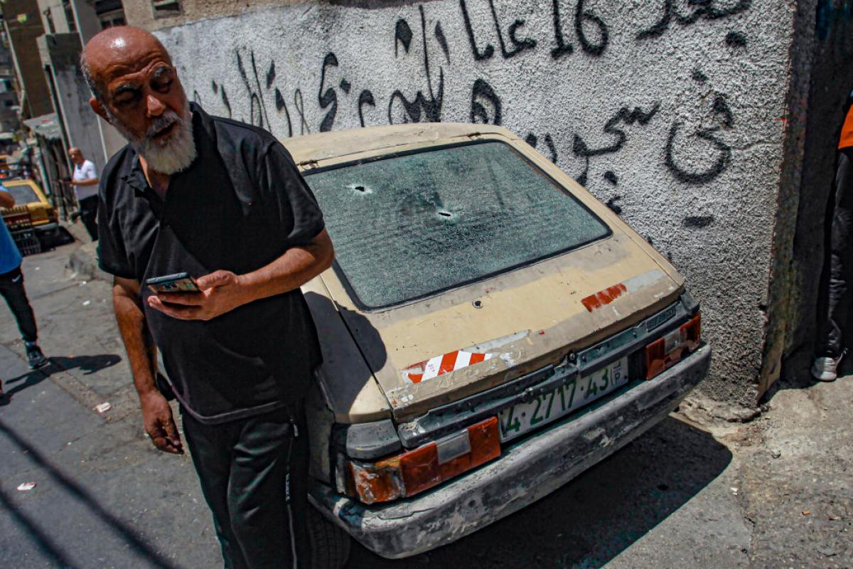 Un palestino, de pie, junto a su vehículo en el que se pueden ver marcas de bala en los cristales.